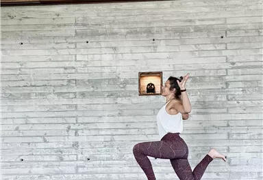 Eine Person macht eine Yoga-Übung auf einer Matte in einem modernen Raum mit Holz- und Steinwänden. Der Hintergrund ist minimalistisch und hell.