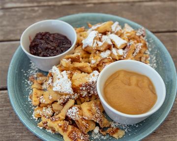 Ein Teller mit knusprigen Waffeln, verziert mit Puderzucker. Dazu zwei Schalen mit Apfelmus und Schokoladensoße.