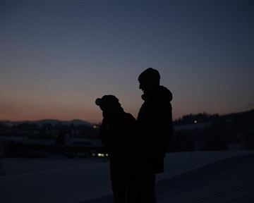 Ein Paar steht in der Dämmerung und betrachtet die Landschaft. Die Silhouetten sind vor einem ruhigen, abendlichen Himmel sichtbar.