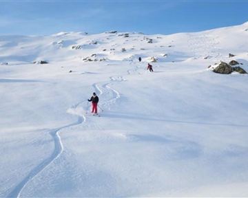Eine verschneite Landschaft mit mehreren Skifahrern. Der Himmel ist klar und blau.