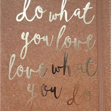 Ein Notizbuch mit dem Motiv „Do what you love, love what you do“ in goldener Schrift. Der Hintergrund ist braun und hebt den Text hervor.