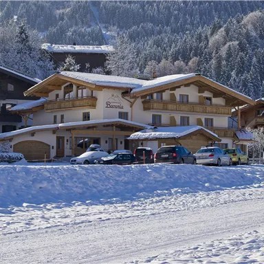 Ein malerisches Chalet im Schnee mit einem klaren blauen Himmel. Im Vordergrund läuft eine Person auf einem verschneiten Weg.