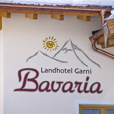 Ein ansprechendes Wandlogo des Landhotels Garni "Bavaria" mit einer Bergsilhouette und einer Sonne. Die warme, einladende Gestaltung vermittelt ein gemütliches Alpenambiente.