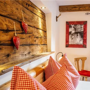 Ein gemütliches Zimmer mit einem Holzpanel und roten Herzen an der Wand. Die Kissen sind kariert in Rot und Weiß, neben einem kleinen Tisch und einem Stuhl.