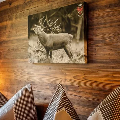 Ein Hirschbild in Schwarz-Weiß hängt an einer Holzwand. Im Vordergrund sind Kissen mit kariertem Muster zu sehen.
