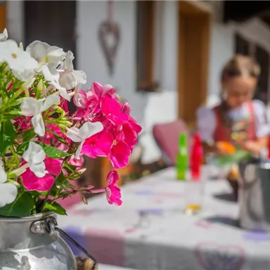 Ein bunten Blumenstrauß in einer Vase steht auf einem Tisch. Im Hintergrund ist ein Kind zu sehen, das mit Essen beschäftigt ist.