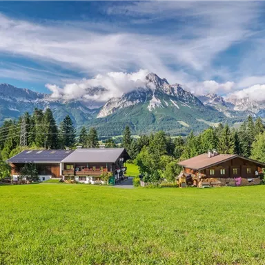 Ein malerisches Bergdorf mit zwei gemütlichen Hütten. Im Hintergrund erheben sich majestätische Berge unter einem klaren Himmel.