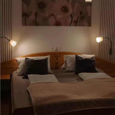 A cozy bedroom with a large bed and soft lighting. On the wall hangs a picture with floral motifs.