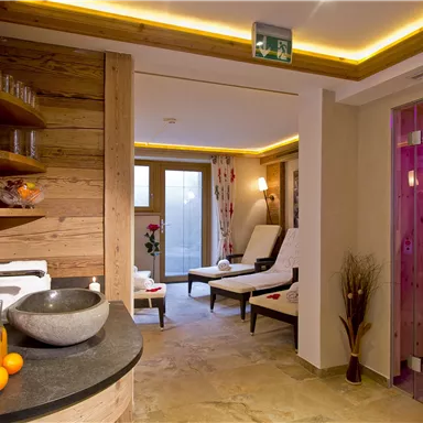 Ein entspannender Spa-Bereich mit Holzverkleidung und sanfter Beleuchtung. Bequeme Liegen und eine moderne Wellness-Dusche laden zur Erholung ein.