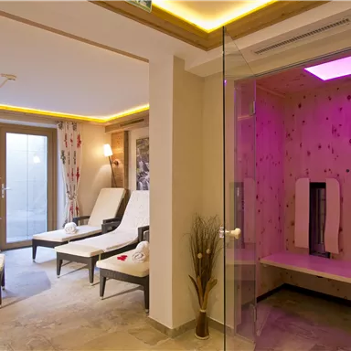 Ein entspannender Wellnessbereich mit Liegen und einer Sauna. Die Atmosphäre ist ruhig und angenehm, mit sanftem Licht und einer modernen Einrichtung.