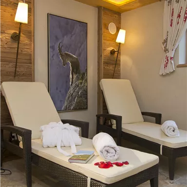 Ein gemütlicher Wellnessbereich mit zwei Liegen aus Rattan. Sanfte Beleuchtung und ein Kunstwerk an der Wand schaffen eine entspannende Atmosphäre.