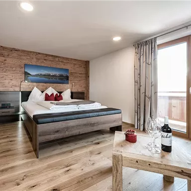 A modern bedroom with wooden walls and a large bed. On the table are wine and glasses as well as a decorative detail.