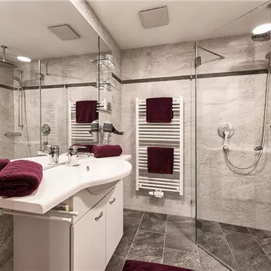 A modern bathroom with a glass shower and elegant gray walls. Burgundy towels and a stylish washbasin give the space a sophisticated touch.