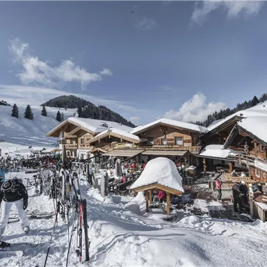 Ein malerisches Bergdorf mit Holzchalets im Schnee. Skifahrer genießen die winterliche Landschaft und die klaren Himmel.