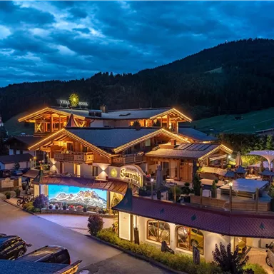 Ein gemütliches Hotel in den Bergen, das abends beleuchtet ist. Die Umgebung zeigt eine schöne Berglandschaft unter einem sternklaren Himmel.