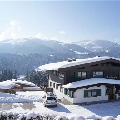 A snow-covered mountain village with traditional houses. In the background, majestic mountains rise under a clear blue sky.