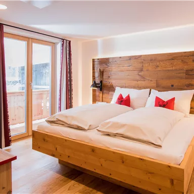 Ein gemütliches Schlafzimmer mit einem großen Bett und Holzdetails. Durch die Fenster gelangt viel Tageslicht hinein.