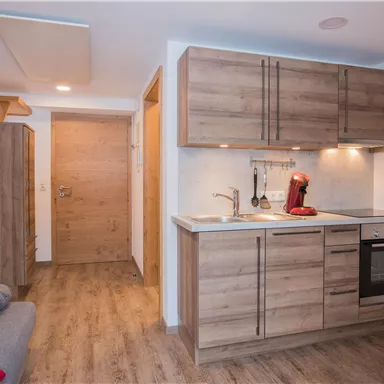 Eine moderne Küche mit Holzschränken und einem Herd. Im Hintergrund ist der Eingang zu sehen.