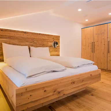 Ein modernes Schlafzimmer mit einem gemütlichen Holzbett und großen Kissen. Der Raum hat einen warmen, einladenden Holzfußboden und eine helle, freundliche Atmosphäre.