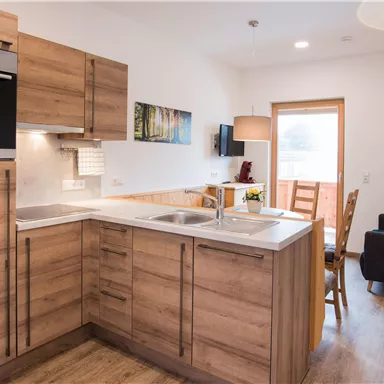 Eine moderne Küche mit Holzschränken und einem eleganten Design. Der Raum ist hell und freundlich mit einem Tisch und Stühlen.