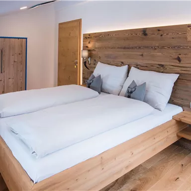 Ein modernes Schlafzimmer mit einem Doppelbett und hellen Holzdetails. Die gemütliche Atmosphäre wird durch die warmen Wandfarben und sanfte Beleuchtung unterstrichen.