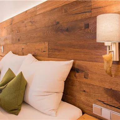 Ein gemütliches Schlafzimmer mit einer Holzvertäfelung und einem weichen Bett. Auf den Kissen liegen grüne Dekokissen, und die Wände sind mit warmem Licht beleuchtet.