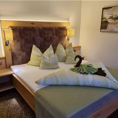 A cozy hotel room with a double bed and decorative cushions. There is soft lighting and an appealing wall design.