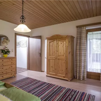 Ein gemütliches Schlafzimmer mit Holzvertäfelung und großen Fenstern. Der Raum ist mit einem Bett, einem Kleiderschrank und einem bunten Teppich ausgestattet.