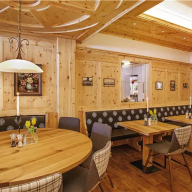 A cozy restaurant with wooden decor and round tables. The walls are decorated with pictures and comfortable benches.