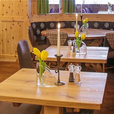 A cozy restaurant with wooden walls and stylishly furnished tables. There are fresh flowers and candles on the tables, creating an inviting atmosphere.