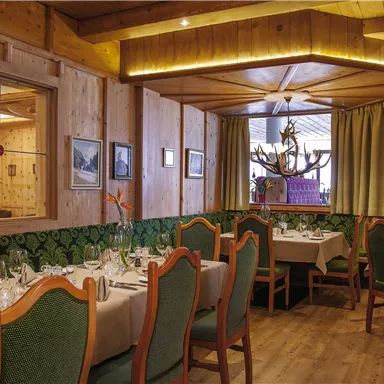 An elegant restaurant with wood paneling and a cozy atmosphere. Tables are beautifully set, and there are large windows with curtains.