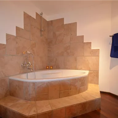 A modern bathroom with a stylish bathtub and an interesting wall design. Towels in orange and blue complement the ambiance.