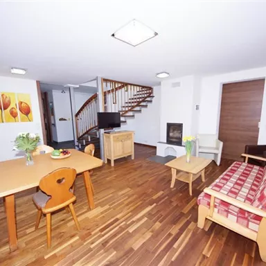 Ein gemütliches Wohnzimmer mit Holzfußboden und treppenaufgang. Es gibt einen Esstisch, eine Couch und einen Fernseher.