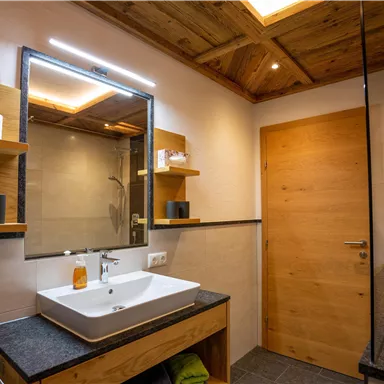 Ein modernes Badezimmer mit Holzregalen und einem Waschbecken auf einem stilvollen Unterschrank. Die Beleuchtung ist sanft und schafft eine angenehme Atmosphäre.