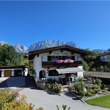 A charming alpine building with colorful flower boxes. In the background, majestic mountains and a bright blue sky are visible.