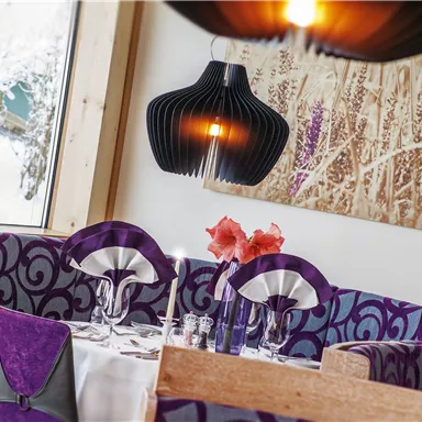 A modern restaurant with purple velvet sofas and stylish lamps. The table is elegantly set and decorated with flowers.