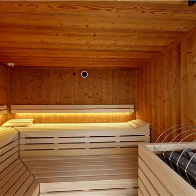A modern sauna with wood paneling and gentle lighting. On the right side, the sauna stones are visible.