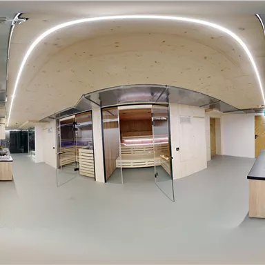 A modern wellness area with wooden saunas and cozy relaxation lounge areas. The room design is bright and inviting with soft lighting elements.