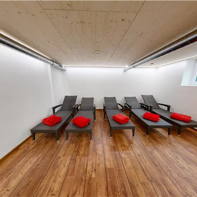 A quiet room with several loungers and red towels. The walls are bright and the floor is made of wood.