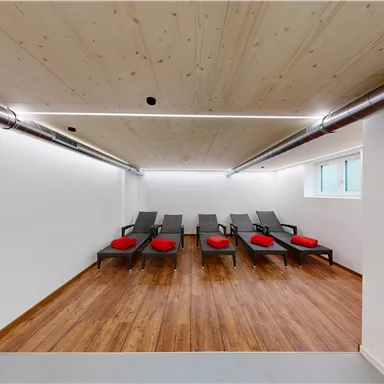 A relaxing room with loungers and red cushions. The walls are bright, the floor is made of wood, and there is pleasant lighting.