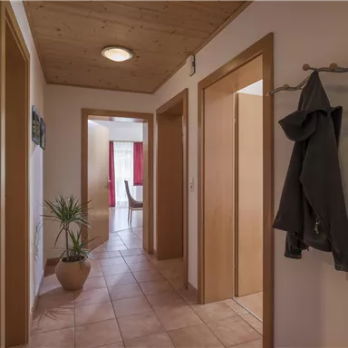 Ein heller Flur mit Holzdecke und Fliesenboden. An der Wand hängen ein Spiegel und eine Kleiderablage.