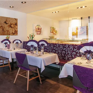 An elegant restaurant with purple decorated tables and chairs. The atmosphere is modern and inviting.
