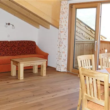 Ein gemütlicher Wohnraum mit einem orangefarbenen Sofa und einem Holzkaffee-Tisch. Große Fenster bieten viel Tageslicht und einen Blick auf den Balkon.