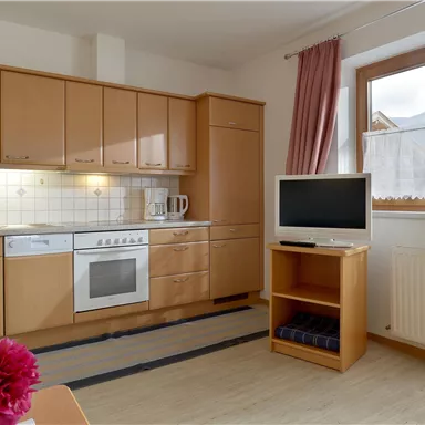 A bright kitchen with wooden cabinets and modern appliances. There is a television in the room and a large window with a view.