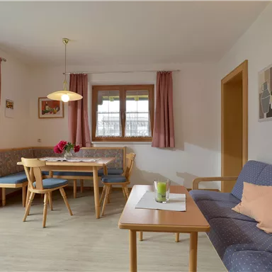 A cozy living room with a seating area and a dining table. Bright walls and large windows create an inviting atmosphere.