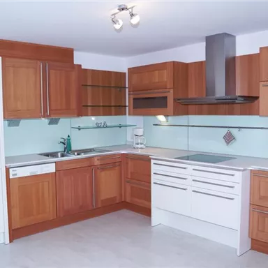 Eine moderne Küche mit Holzschränken und hellen Wänden. Sie verfügt über verschiedene Elektrogeräte und eine klare, funktionale Anordnung.