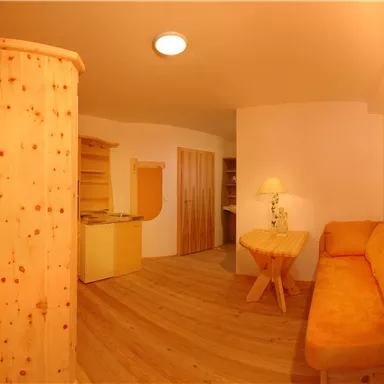 A cozy room with an orange sofa and wooden furniture. The atmosphere is warm and inviting, with a wooden floor.