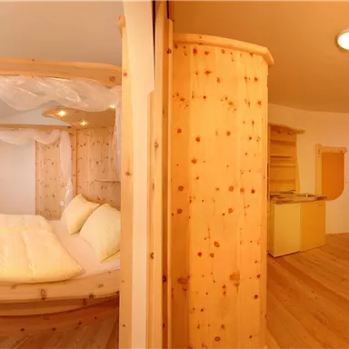 A modern room with a round wooden bed and a cozy living area. The warm colors and bright light create an inviting atmosphere.