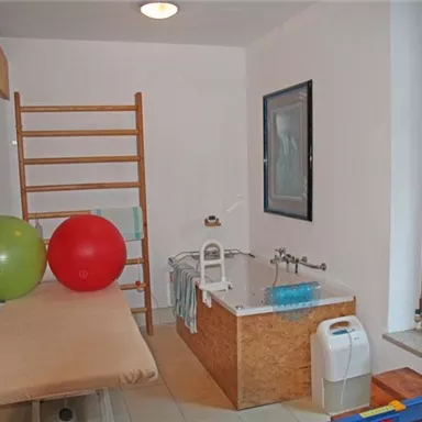 A modern bathroom with a bathtub and colorful fitness balls. There is also a shelf and large windows that let in light.