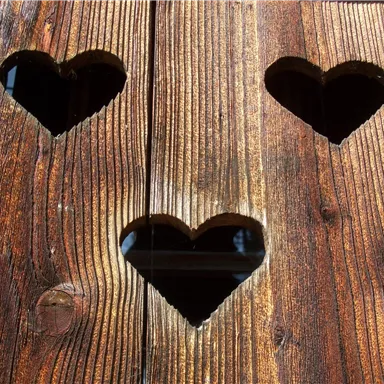 Three heart-shaped openings in a rustic wooden wall. The light gently shines through the hearts.